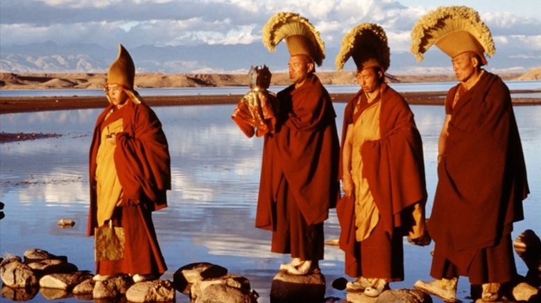 Gyurme Tethong as the Dalai Lama stands with other Lamas on rocks surrounded by water in Kundun