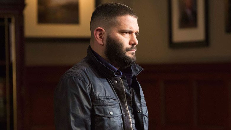 Huck in a black jacket looking taciturn in the OPA offices on Scandal