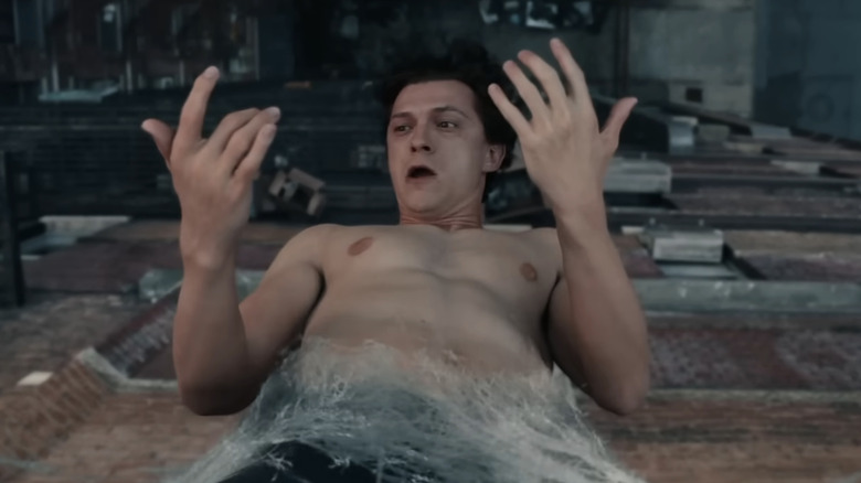 Tom Holland as Peter Parker confused by shooting web from his wrists, hanging from a fire escape in Spider-Man: Brand New Day