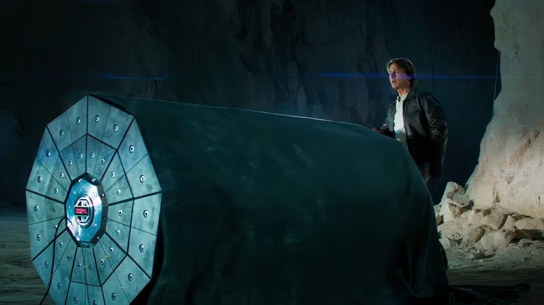 Ethan Hunt stands behind a massive bomb that he has uncovered with a large cloth blanket