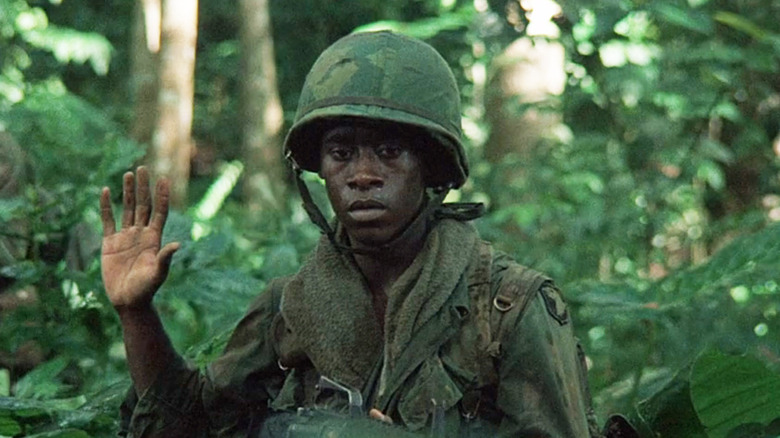 Don Cheadle's Johnny Washburn stands in the jungle with his hand up in Hamburger Hill