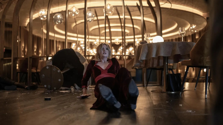 Violet on the floorm backing away from a broken window in the movie Drop.