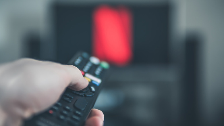 A hand holding a remote control turns on the Netflix streaming app on a home television.