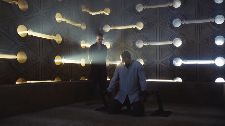 Paul Atreides stands in the corner of a futuristic looking room, looming over Duncan Idaho, who is on his knees, in Dune: Chapter Three