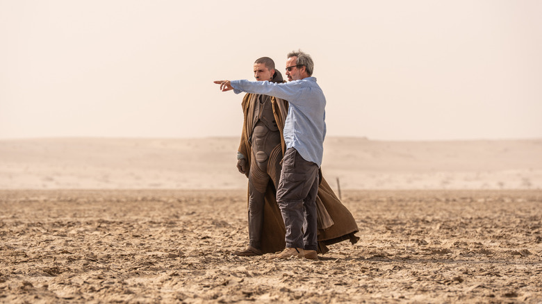 Director Denis Villeneuve pointing to the horizon next to Timotheé Chalamet as Paul Atreides in a desert on the set of Dune: Part Three
