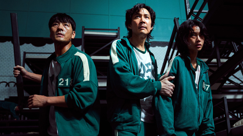 three men in green jumpsuits looking alert in a gym