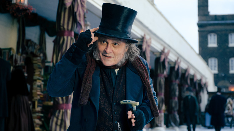 Ebenezer Scrooge (Johnny Depp) tips his hat on a snowy street.