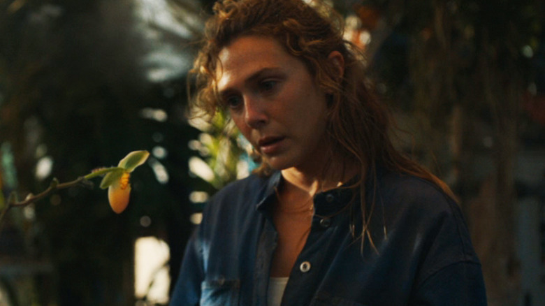 Elizabeth Olsen as Mia stands amidst plants in The Assessment