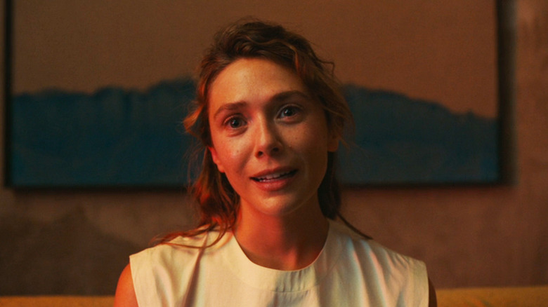 Elizabeth Olsen as Mia is seen in closeup against a plain wall with a painting on it in The Assessment