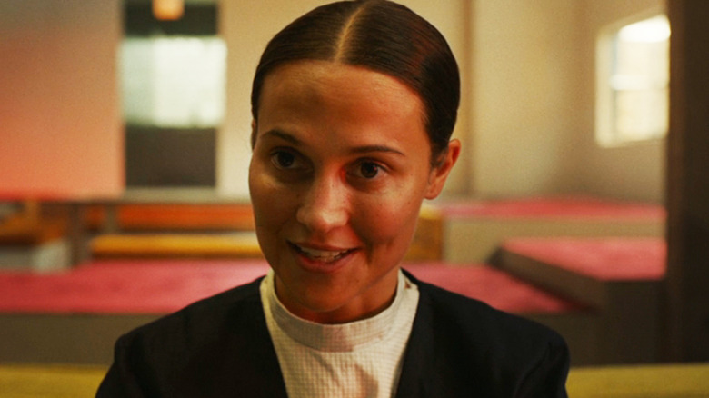Alicia Vikander as Virginia is seen in closeup as she sits in a living room in The Assessment