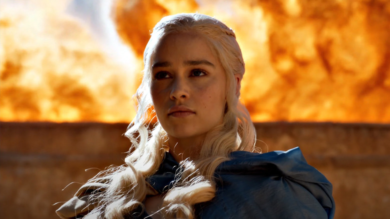 Emilia Clarke as Daenerys Targaryen standing in front of a wall of fire in Game of Thrones