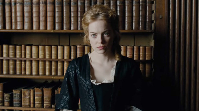 Abigail Hill sitting in front of a bookshelf in The Favourite
