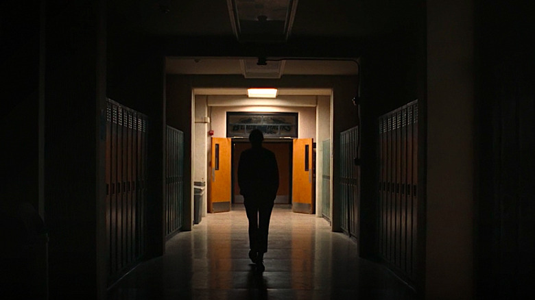 Rue walks down a dark school hallway