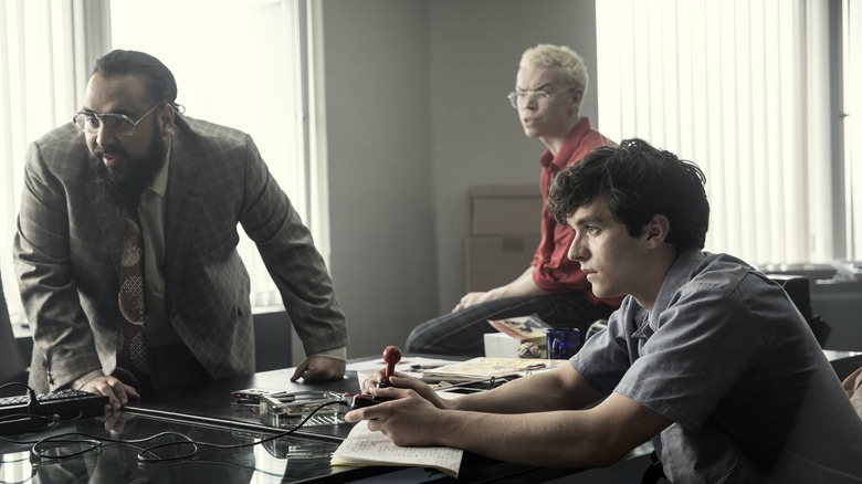 Stefan (Fionn Whitehead) demonstrates game to Mohan Thakur (Asim Chaudhry) and Colin Ritman (Will Poulter) in Black Mirror: Bandersnatch