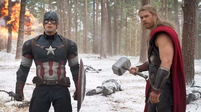 Steve Rogers (Chris Evans) and Thor (Chris Hemsworth) stand in a snowy forest with fire behind in Avengers: Age of Ultron