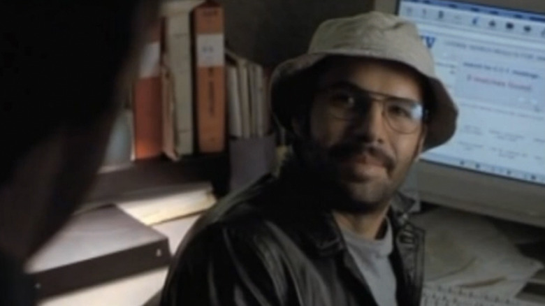 Billy Zane as Joe, sitting at a computer wearing a bucket hat and looking at someone off screen