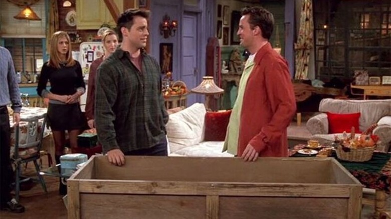 Joey Tribbiani (Matt LeBlanc) and Chandler Bing (Matthew Perry) talk next to a large crate as Rachel Green (Jennifer Aniston) and Phoebe Buffay (Lisa Kudrow) watch