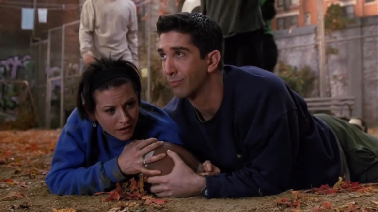 Monica Geller (Courteney Cox) and Ross Geller (David Schwimmer) lay on the ground holding a football in Friends