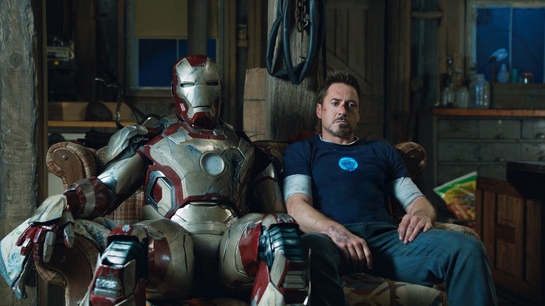 Tony sitting next to his Iron Man suit on a couch in Iron Man 3