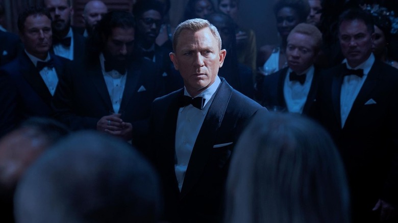 Daniel Craig as James Bond surrounded by a crowd in tuxedos in No Time To Die