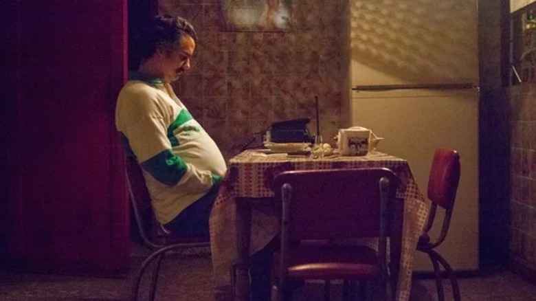 Wagner Moura as Pablo Escobar sitting at a table while looking sad on Narcos