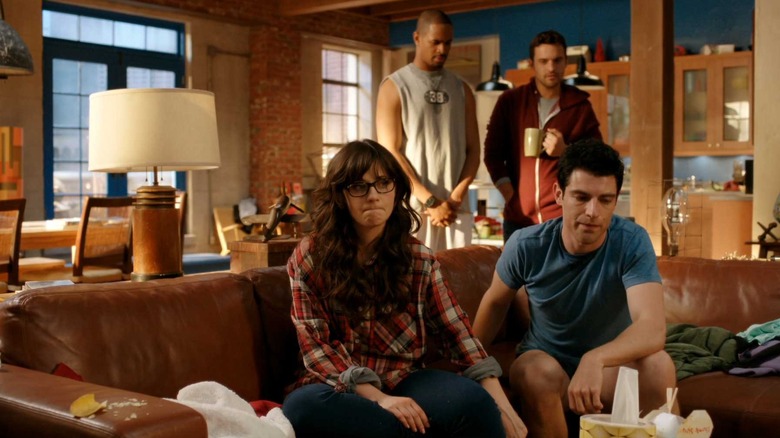 Jess and Schmidt sitting on the loft's couch with Coach and Nick behind them on New Girl