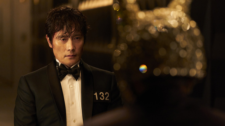 In-ho in a tuxedo with 132 on his chest talking to a VIP in Squid Game
