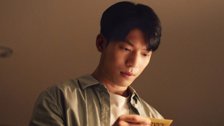 Jun-ho looking down at a Squid Game invitation card on Squid Game