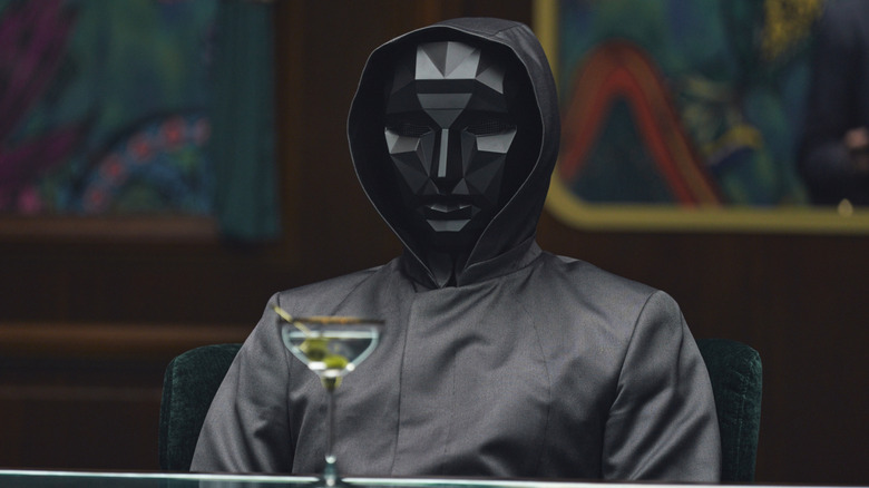 The Front Man in a mask with a drink in front of him on Squid Game