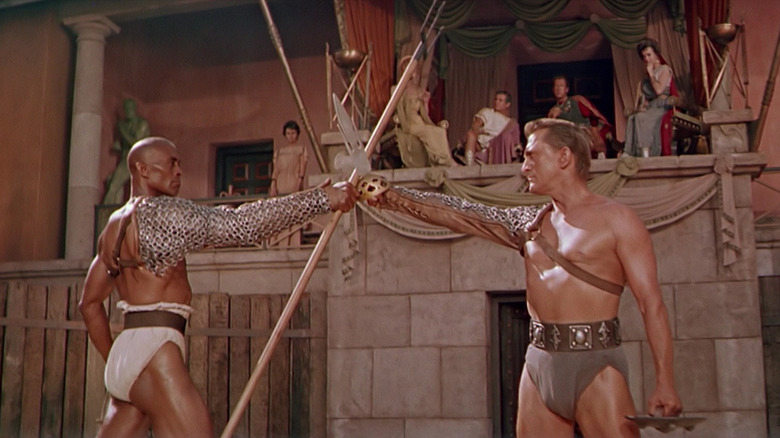 Spartacus (Kirk Douglas) holds a sword up to a warrior holding a long pitchfork in Spartacus