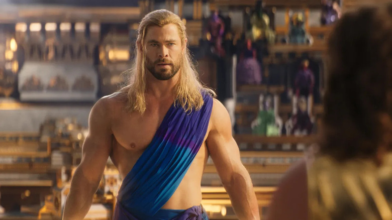 Thor (Chris Hemsworth) stands with a revealing sash on in Thor: Love and Thunder