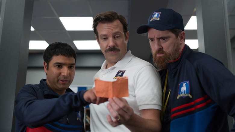 three men in soccer coaching uniforms looking at an orange piece of paper