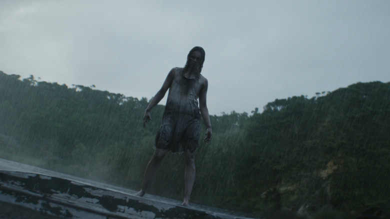 A possessed woman stands by a lake in the rain in Evil Dead Burn