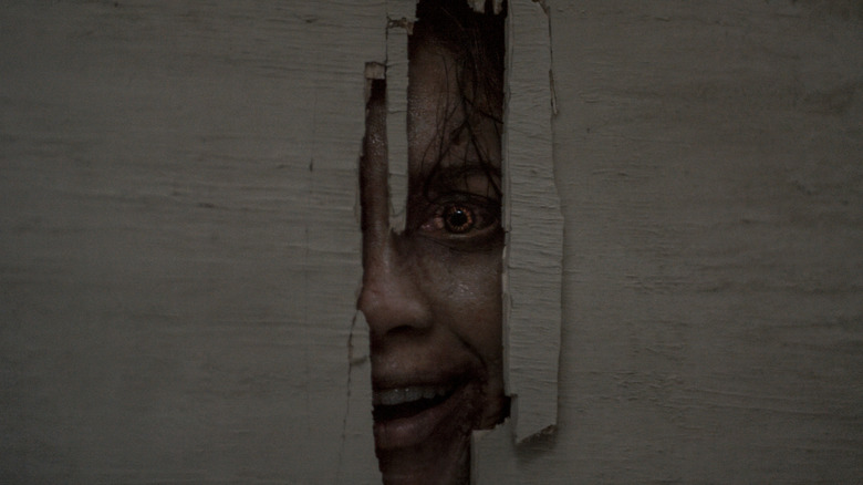 A possessed Thya peeks through a hole in a door in Evil Dead Burn