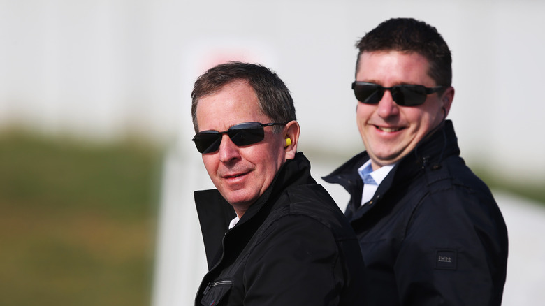 Martin Brundle and David Croft smiling outside in coats and sunglasses