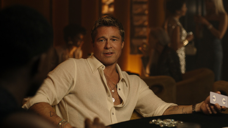 Brad Pitt as racer Sonny Hayes seated at a lounge and holding a playing card in his hand in F1: The Movie