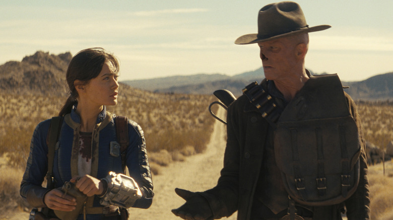 Walton Goggins as The Ghoul reaching out his hand to Ella Purnell as Lucy MacLean as they travel down a dirt road in Fallout