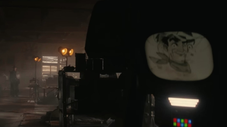 Walton Goggins as The Ghoul standing in the background looking at Jesse Burch as the voice of Victor emerging from the shadows in Fallout