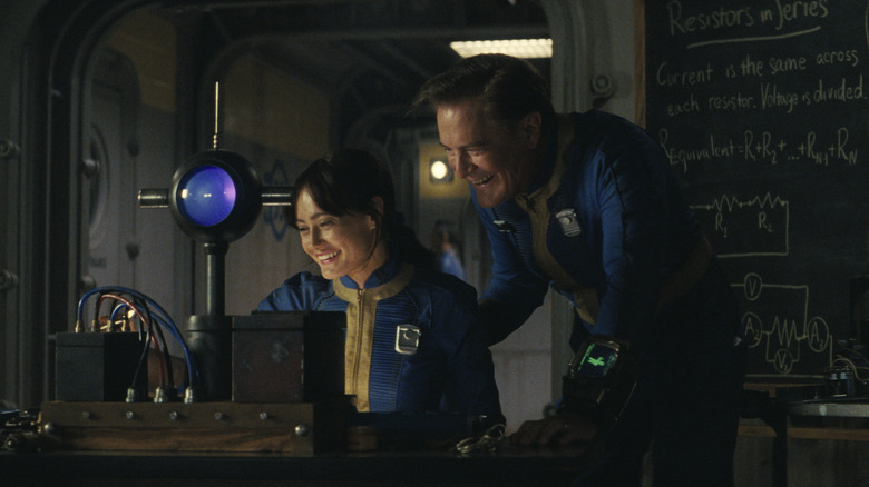 Ella Purnell as Lucy MacLean seated at a desk and laughing with Kyle MacLachlan as Hank MacLean behind her in a classroom in Fallout