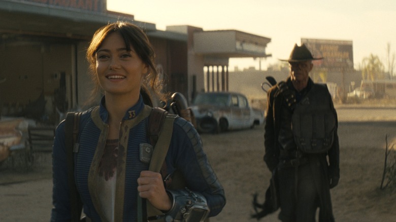 Lucy smiling while the Ghoul walks behind her in Fallout
