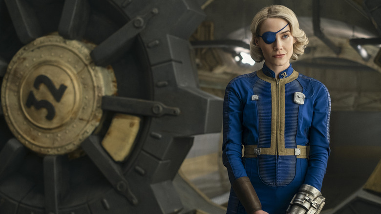 Annabel O'Hagan as Overseer Steph Harper smiling next to a vault door in Fallout