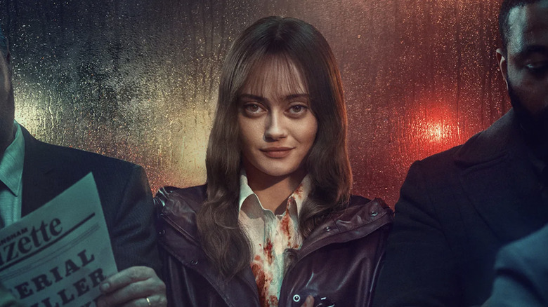 Rhiannon Lewis sitting at the back of a bus, smiling, with blood on her shirt in Sweetpea