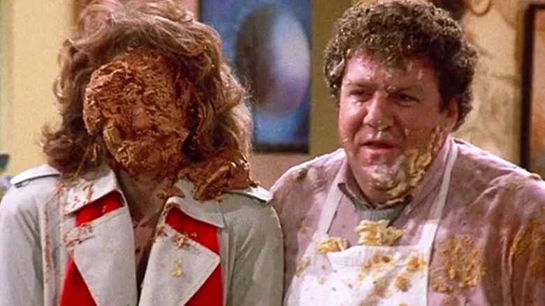 Vera from Cheers standing next to Norm with a pie in her face