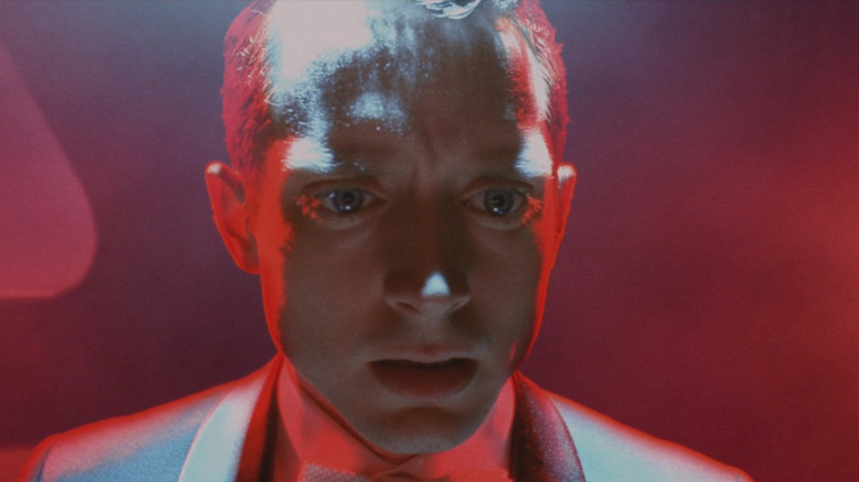 Elijah Wood as Tom Selznick, bathed in red light, terrified air at the tail piano