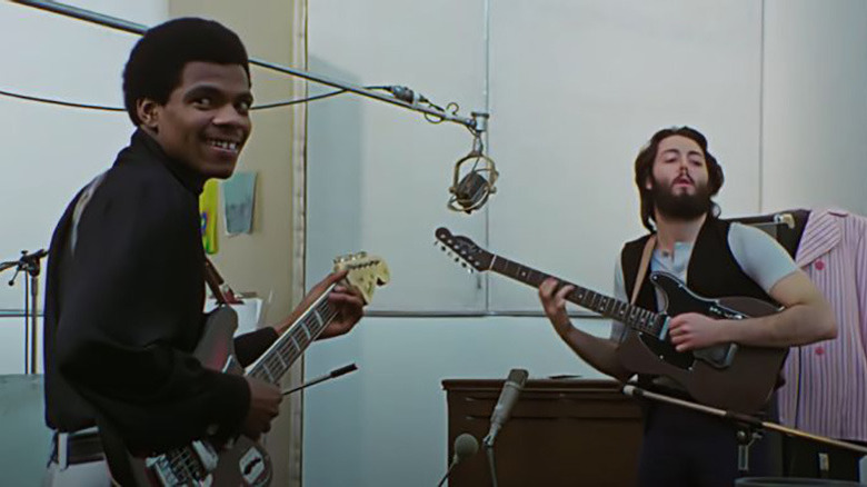 man with guitar looking at camera next to another man with guitar looking up and off-camera