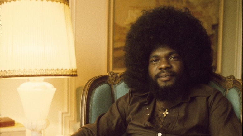 man with an afro sitting down next to a lamp