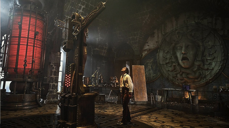 Victor Frankenstein looks up at his future creation on a cross-like object in his lab in Frankenstein (2025)