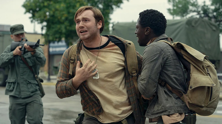 Pete McVries pulls back Ray Garraty as a soldier points a gun at them in The Long Walk