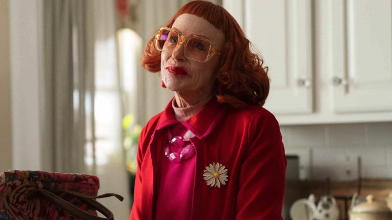 Gladys (Amy Madigan) smiles in a red wig and heavy makeup in a kitchen in Weapons