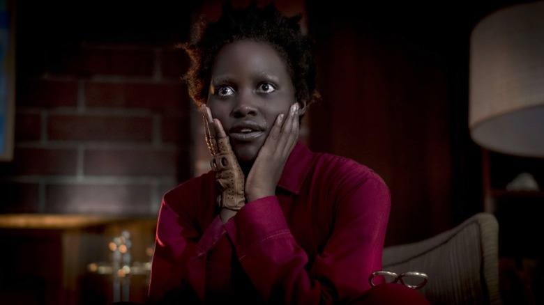 A woman dressed all in red sits down and holds her head in her hands as she looks excitedly off camera.
